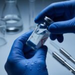 Rischio chimico: Immagine macro dettagliata di mani che indossano guanti protettivi in nitrile blu mentre maneggiano un contenitore di solvente liquido, gocce di liquido sulla superficie, illuminazione da laboratorio fredda, realismo estremo sui materiali.